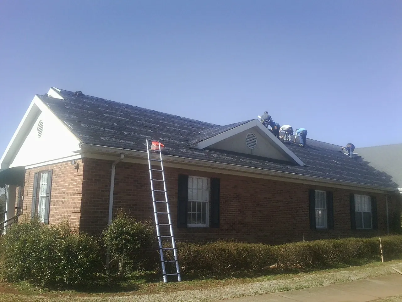 Crew tearing shingles off a brick ranch roof with a ladder set — Emergency Roof Repair work by our crew in Tres Pinos