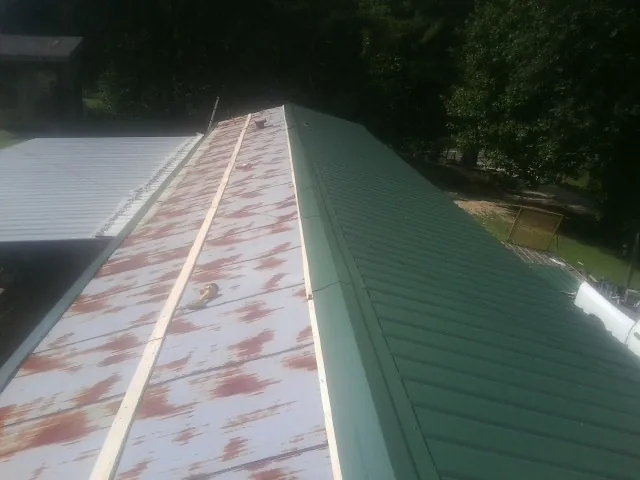 Old rusted panels beside newly installed green metal roofing — Wind Damage Roof Repair by Roofing Brothers in Tres Pinos