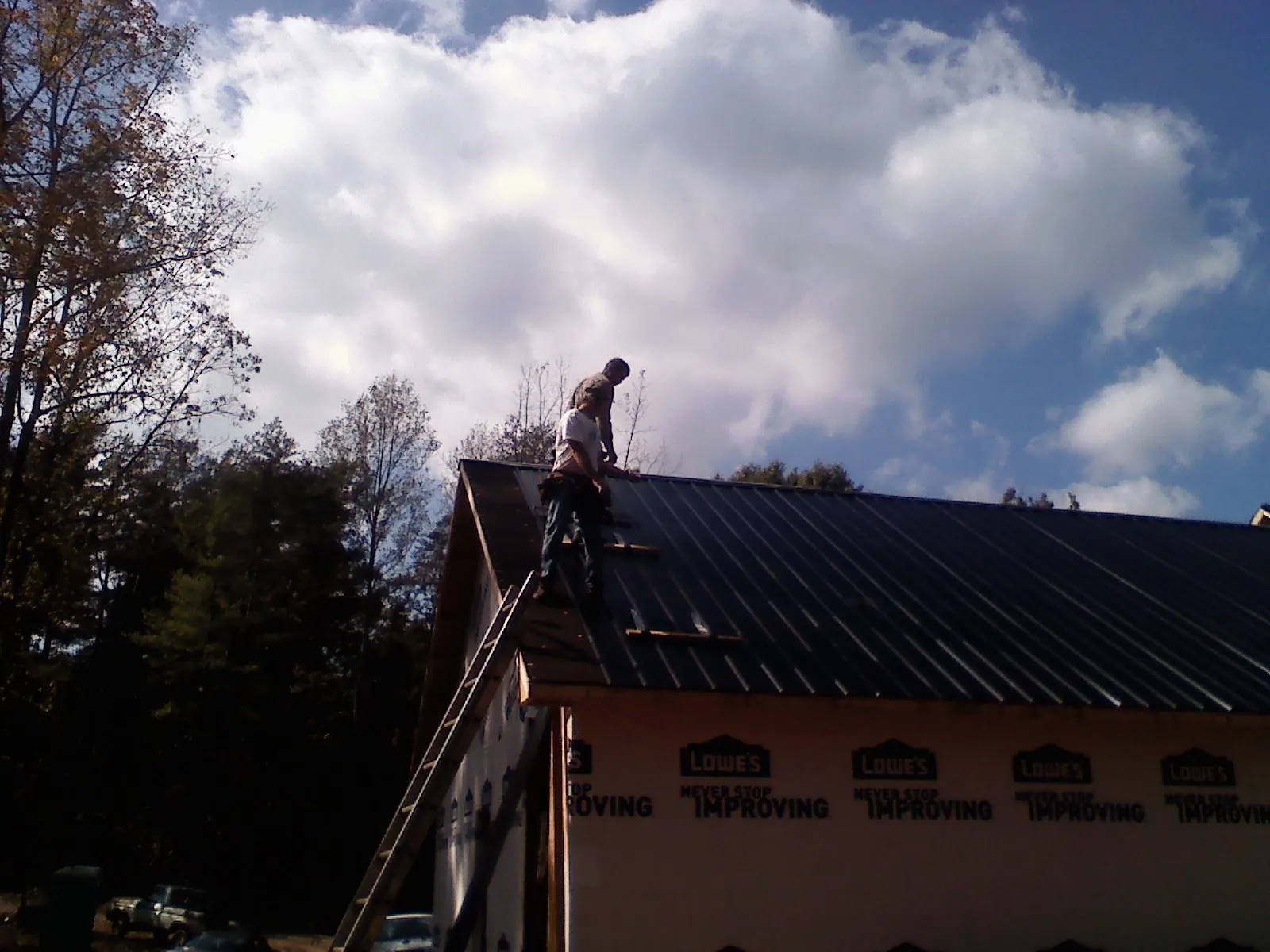 Roofer fastening dark metal panels high against a cloudy sky, from a Roof Inspection job in Tres Pinos