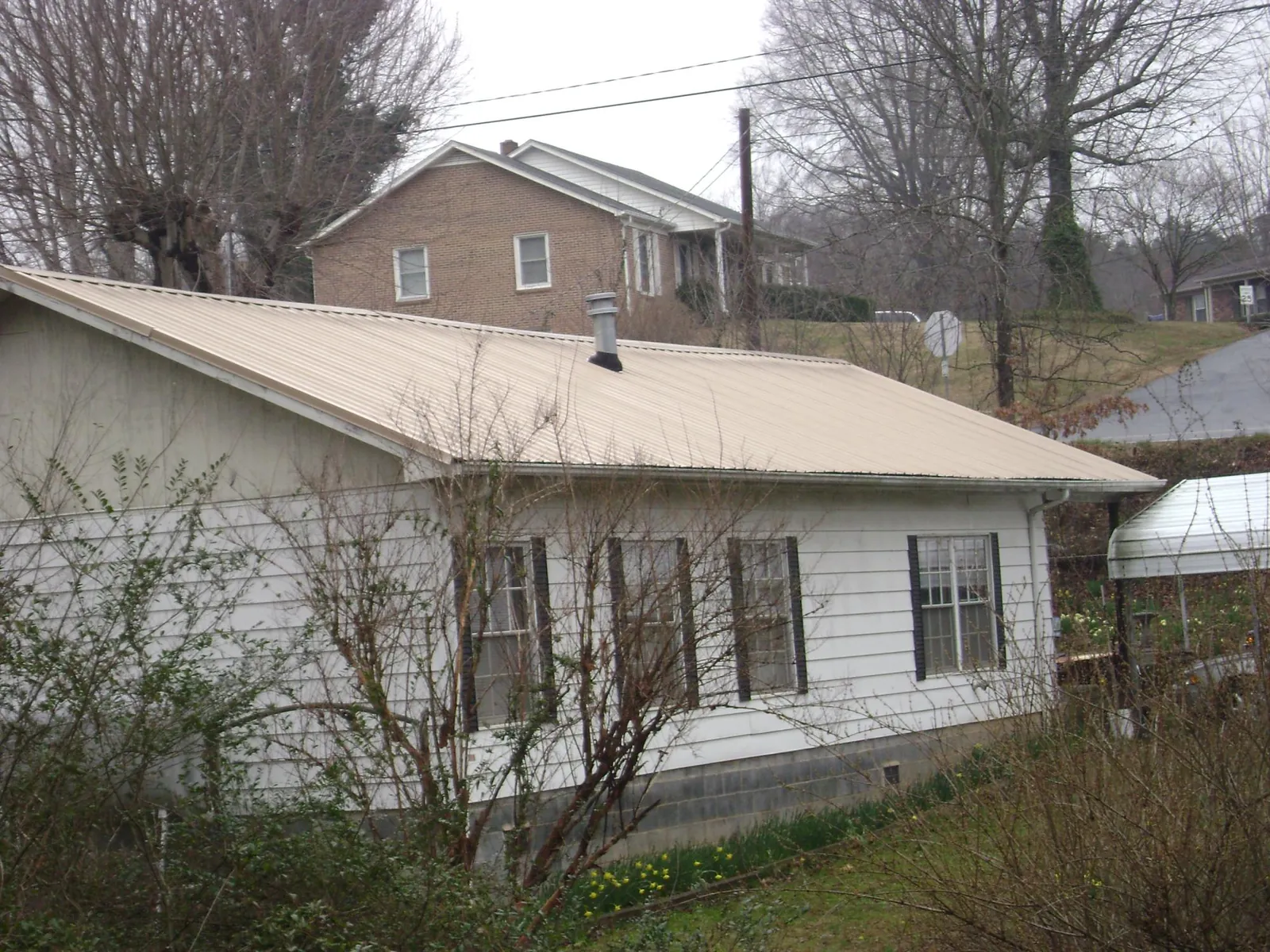 Tan metal roof on a white sided house set into a hillside — Commercial Roofing by Roofing Brothers in Tres Pinos